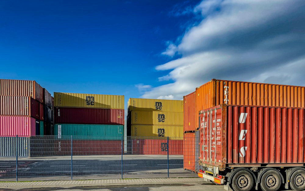 Lorry parked in front of stacked shipping containers